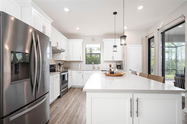 kitchen with appliances with stainless steel finishes, hanging light fixtures, backsplash, white cabinets, and a kitchen island