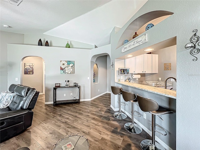 kitchen with dark wood-type flooring, a breakfast bar, light stone counters, vaulted ceiling, and white cabinets