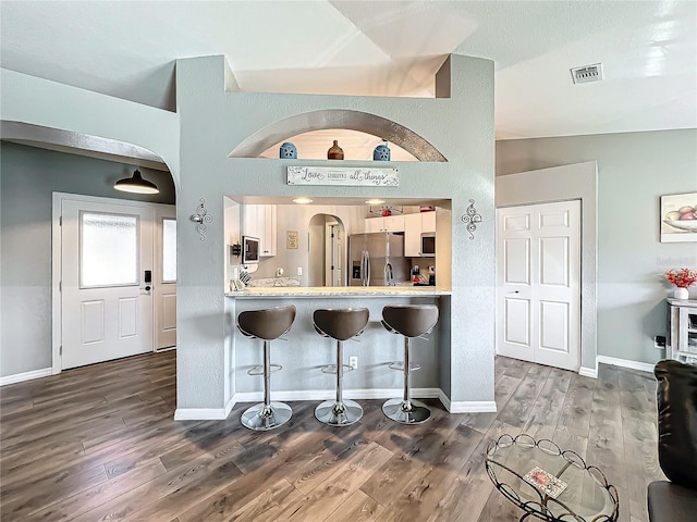 kitchen featuring dark hardwood / wood-style floors, lofted ceiling, a kitchen bar, kitchen peninsula, and stainless steel appliances