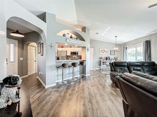 living room featuring an inviting chandelier, wood-type flooring, and vaulted ceiling