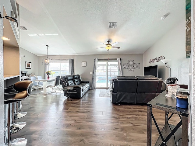 living room featuring ceiling fan with notable chandelier, dark hardwood / wood-style floors, a wealth of natural light, and a textured ceiling