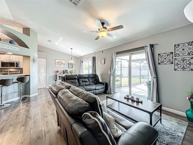 living room featuring ceiling fan, light hardwood / wood-style floors, vaulted ceiling, and a textured ceiling