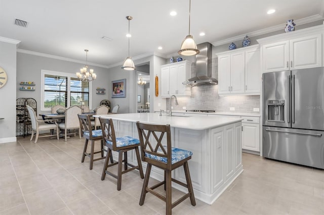 kitchen with wall chimney exhaust hood, sink, white cabinets, a center island with sink, and high quality fridge