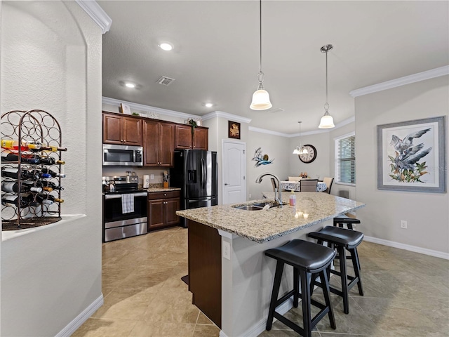 kitchen featuring sink, hanging light fixtures, light stone countertops, appliances with stainless steel finishes, and a breakfast bar area