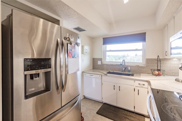 kitchen featuring white cabinetry, stainless steel appliances, tasteful backsplash, sink, and a tray ceiling