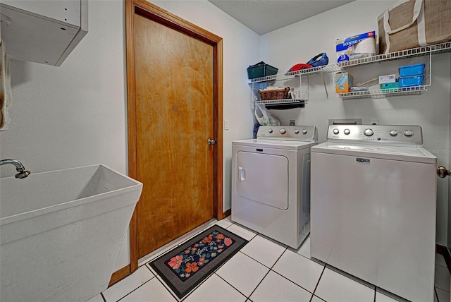 laundry room featuring sink, washing machine and clothes dryer, a textured ceiling, and light tile patterned flooring