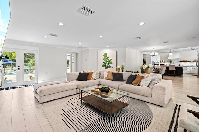 living room with french doors, crown molding, a chandelier, and light hardwood / wood-style flooring