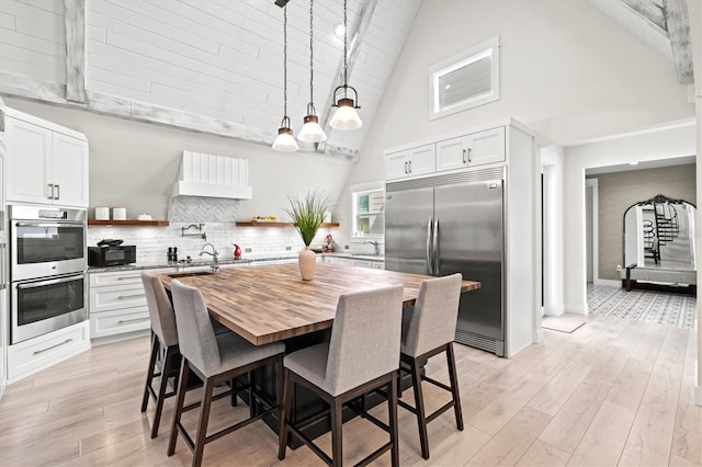 kitchen featuring pendant lighting, tasteful backsplash, white cabinets, stainless steel appliances, and a center island with sink