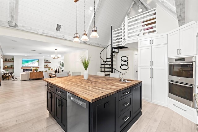 kitchen with high vaulted ceiling, white cabinetry, hanging light fixtures, a center island with sink, and an inviting chandelier