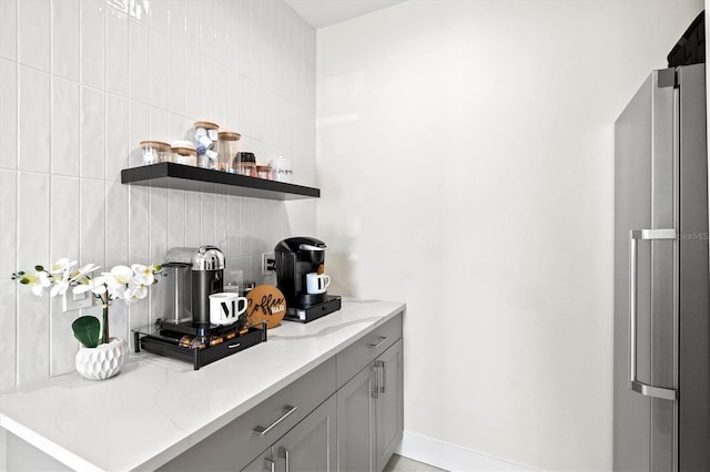 bar with light stone countertops, gray cabinetry, and stainless steel refrigerator