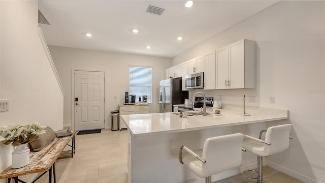 kitchen with white cabinetry, appliances with stainless steel finishes, a kitchen breakfast bar, and kitchen peninsula