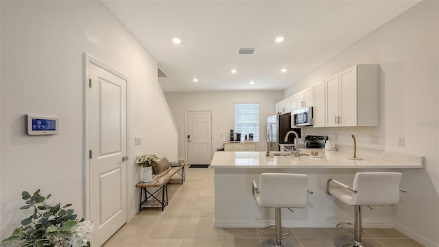 kitchen featuring light tile patterned floors, a kitchen breakfast bar, kitchen peninsula, and appliances with stainless steel finishes