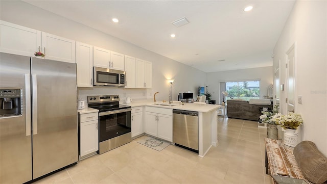 kitchen with white cabinetry, kitchen peninsula, appliances with stainless steel finishes, and sink