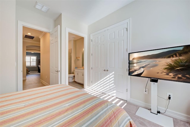 bedroom with crown molding, ensuite bath, light colored carpet, and a closet