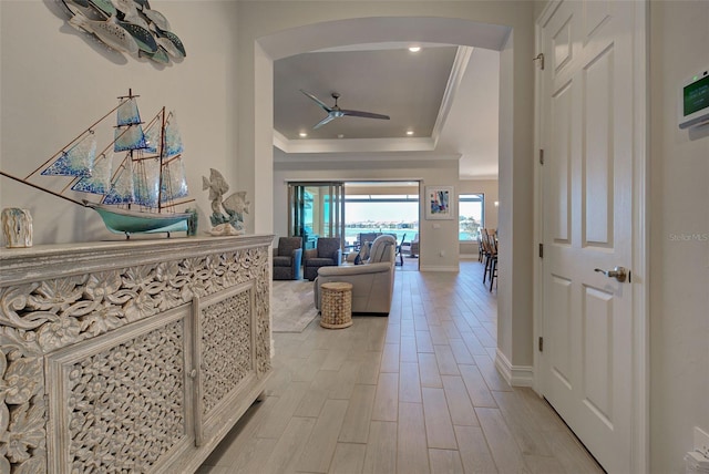 hall featuring light hardwood / wood-style flooring, ornamental molding, and a raised ceiling