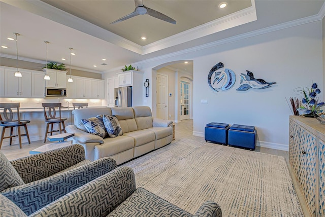 living room featuring a tray ceiling, light hardwood / wood-style flooring, ornamental molding, and ceiling fan