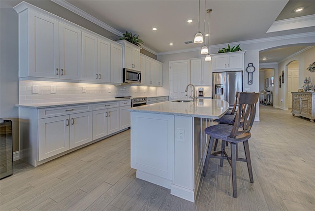 kitchen with appliances with stainless steel finishes, pendant lighting, sink, white cabinets, and a kitchen island with sink