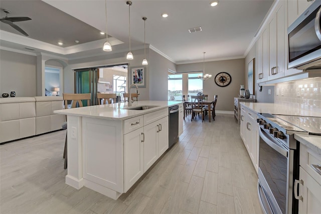 kitchen featuring sink, pendant lighting, stainless steel appliances, a kitchen island with sink, and white cabinets