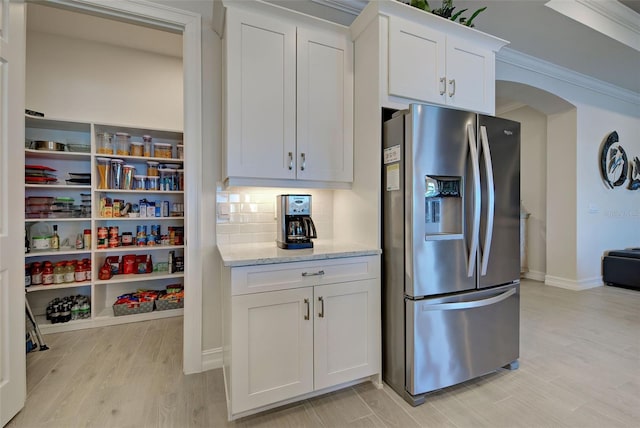 kitchen featuring white cabinetry, light wood-type flooring, stainless steel fridge, light stone countertops, and decorative backsplash