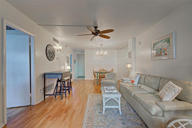 living room with a textured ceiling, ceiling fan with notable chandelier, and light hardwood / wood-style floors