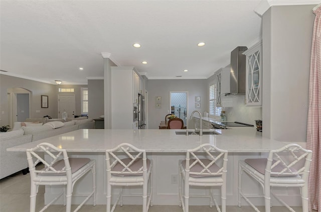 kitchen with light stone counters, kitchen peninsula, wall chimney exhaust hood, and a breakfast bar area