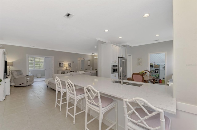 kitchen with appliances with stainless steel finishes, a kitchen breakfast bar, light stone countertops, white cabinets, and sink