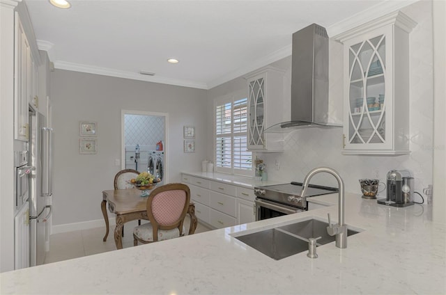 kitchen with backsplash, wall chimney range hood, crown molding, washer and clothes dryer, and appliances with stainless steel finishes