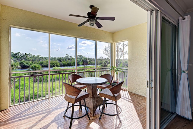 sunroom featuring ceiling fan and a water view