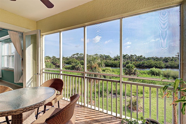 sunroom with ceiling fan and a water view