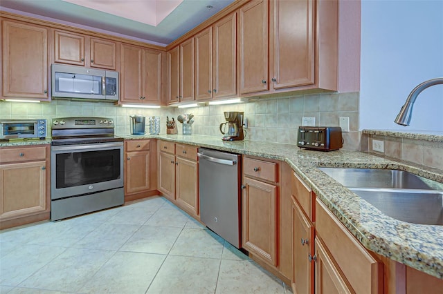 kitchen with light tile patterned floors, stainless steel appliances, decorative backsplash, light stone countertops, and sink