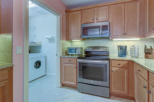 kitchen featuring washer / dryer, decorative backsplash, appliances with stainless steel finishes, light tile patterned floors, and light stone counters