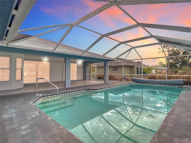 pool at dusk with glass enclosure and a patio area