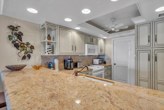 kitchen featuring white appliances, light stone countertops, a raised ceiling, decorative backsplash, and kitchen peninsula