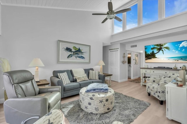 living room with a high ceiling, ceiling fan, and light wood-type flooring