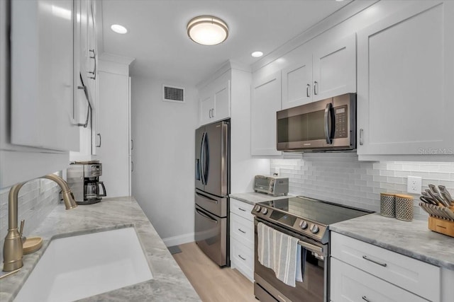 kitchen with sink, appliances with stainless steel finishes, white cabinetry, tasteful backsplash, and light stone countertops