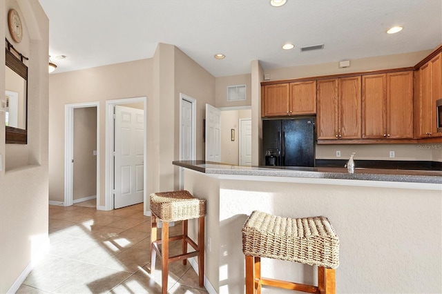 kitchen with a breakfast bar, black fridge with ice dispenser, kitchen peninsula, and light tile patterned floors