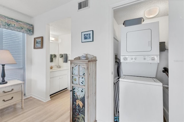 laundry room featuring a textured ceiling, stacked washer / drying machine, and light hardwood / wood-style flooring