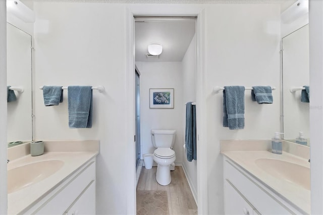 bathroom featuring hardwood / wood-style flooring, toilet, vanity, and a shower with door