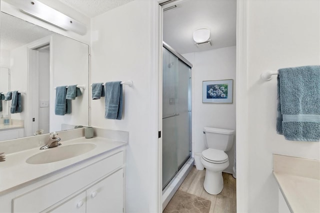 bathroom with toilet, a textured ceiling, a shower with door, and vanity