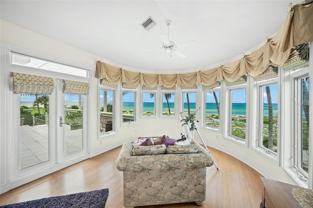 sunroom with ceiling fan, a water view, a view of the beach, and a wealth of natural light