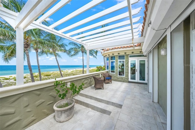 view of patio / terrace featuring a beach view, a balcony, a water view, and a pergola