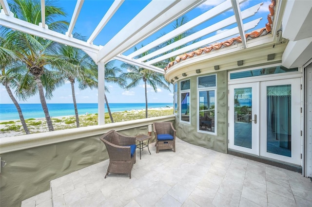 sunroom / solarium featuring french doors, a water view, and a view of the beach