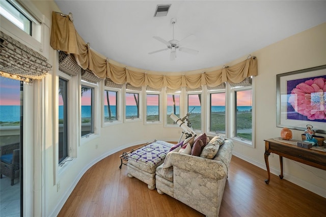 living area featuring ceiling fan, wood-type flooring, a water view, and a healthy amount of sunlight