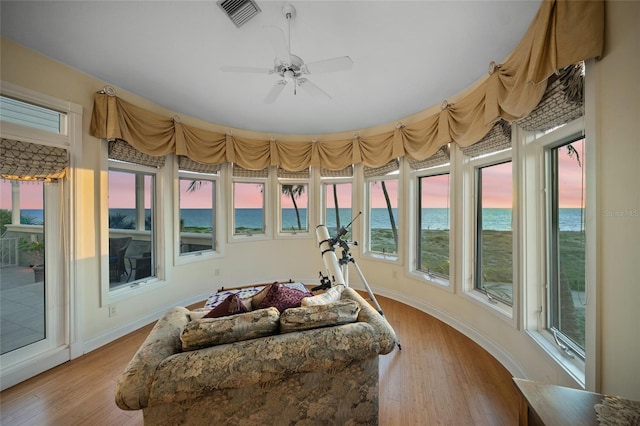 sunroom / solarium with ceiling fan, a beach view, a water view, and a healthy amount of sunlight