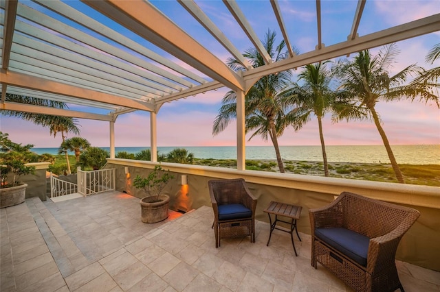 patio terrace at dusk with a beach view, a water view, and a pergola