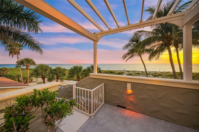 patio terrace at dusk with a balcony, a water view, and a beach view