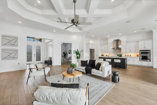 living room featuring a towering ceiling, light wood-type flooring, visible vents, and ornamental molding