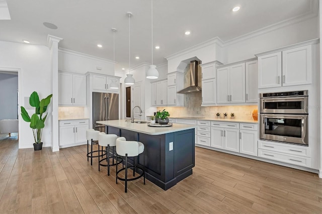 kitchen featuring a breakfast bar, light countertops, appliances with stainless steel finishes, a sink, and wall chimney range hood