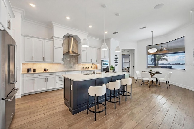 kitchen with stainless steel appliances, tasteful backsplash, light countertops, wall chimney range hood, and light wood-type flooring