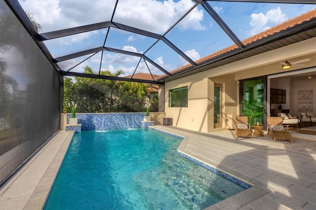 view of pool with glass enclosure, ceiling fan, pool water feature, and a patio